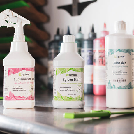 Three bottles of Sgreen screen printing supplies displayed on a workbench, including Supreme Wash, Sgreen Stuff, and Adhesive. The clean and eco-friendly packaging highlights products designed for ink removal, screen cleaning, and pallet adhesion, essential for maintaining quality in the screen printing process.