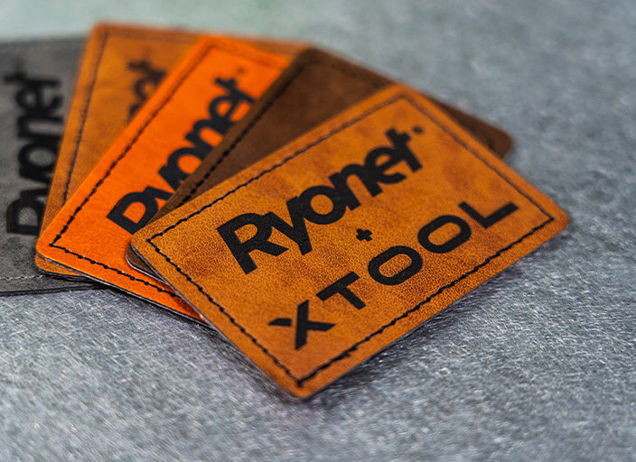 Stack of engraved leather patches featuring the Ryonet + xTool logo in various shades of brown and orange. The clean, precise engraving and stitched edges highlight the quality and craftsmanship of custom leather branding.