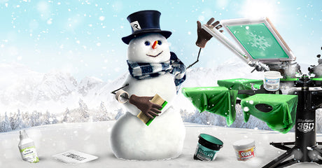 Festive winter scene featuring a cheerful snowman wearing a top hat with an 'R' logo, a scarf, and gloves, holding a squeegee. A Riley Hopkins 360 screen printing press is set up beside the snowman with a green shirt being printed with a snowflake design. Screen printing supplies, including inks and cleaning products, are displayed in the snowy foreground. The background showcases a snowy mountain landscape with falling snow and frosty pine trees, creating a holiday-themed atmosphere.