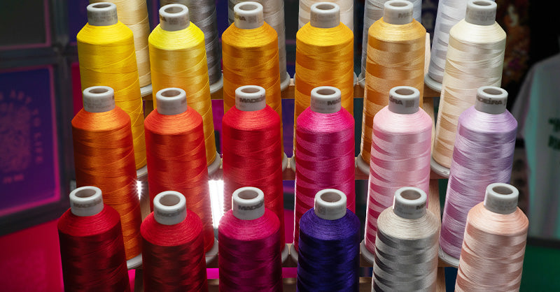 Rows of colorful embroidery thread spools neatly arranged, featuring a range of vibrant hues from reds and oranges to purples and pastels. The shiny threads highlight the variety of options available for creating detailed and eye-catching embroidery designs.